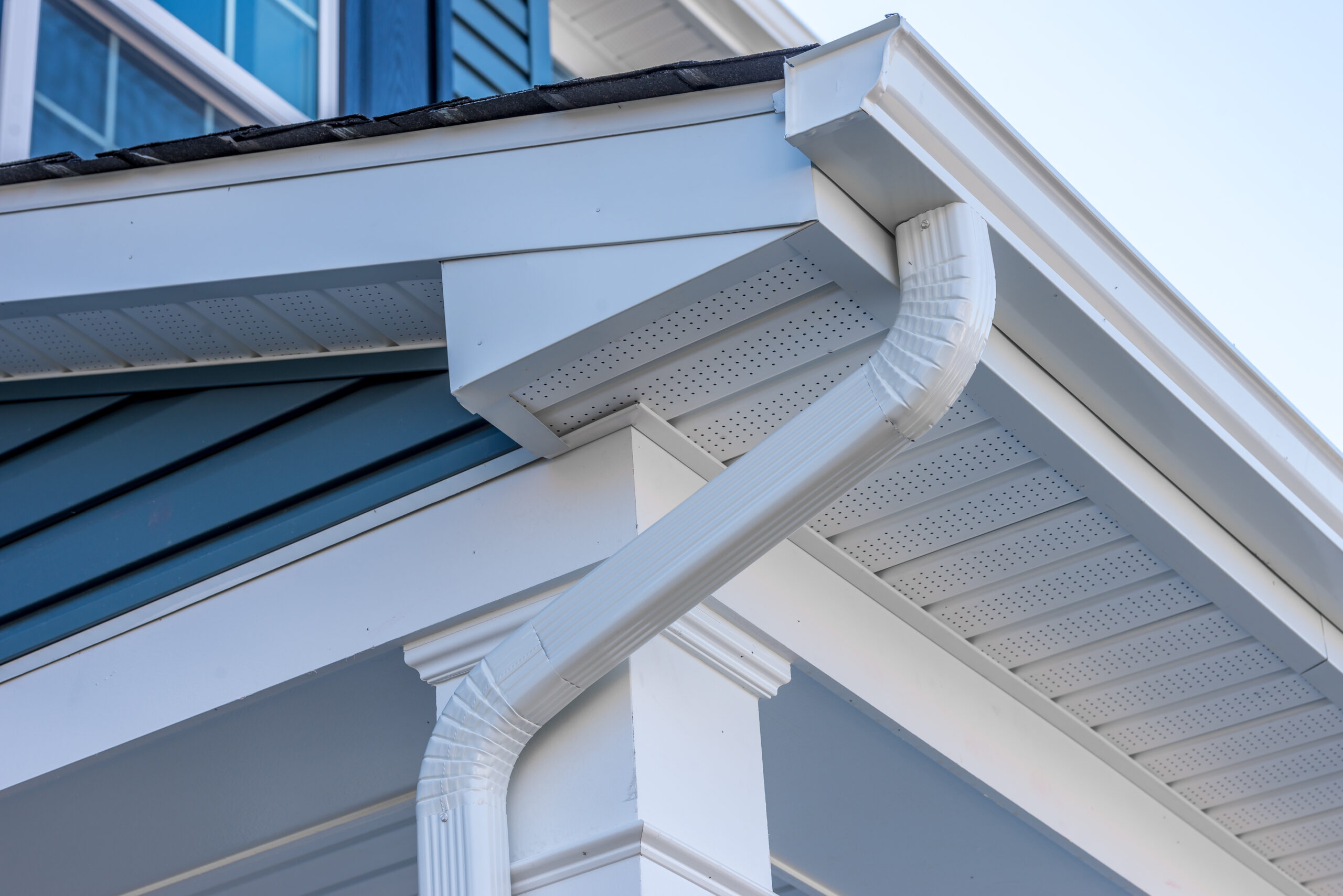 Colonial white gutter guard system, fascia, drip edge, soffit providing ventilation to the attic, with pacific blue vinyl horizontal siding at a luxury American single family home neighborhood USA Gutter installation